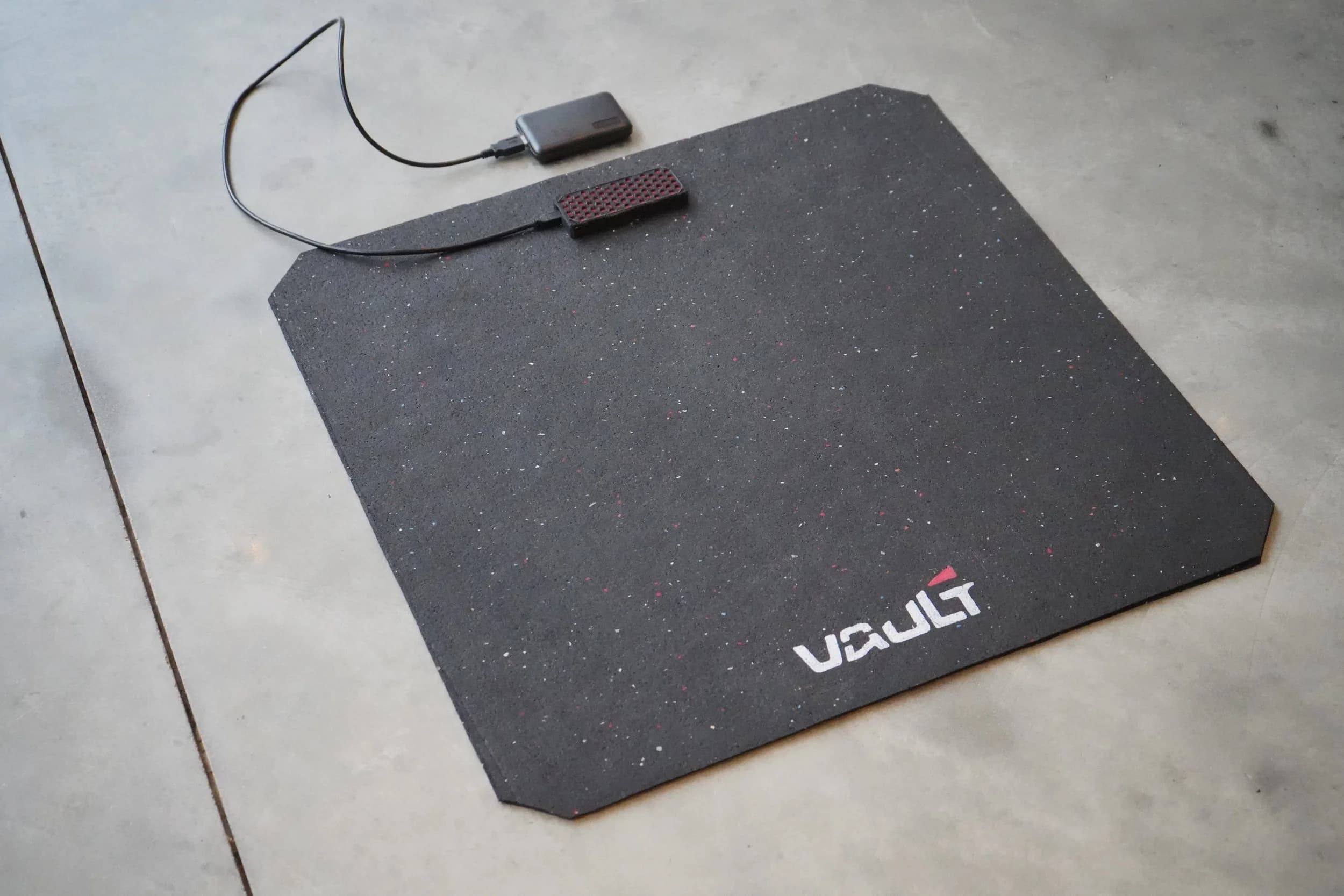 A Vault force platform on a concrete floor, wired to its sensor module and battery.